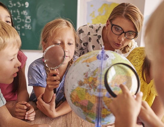 Teacher and children examining globe with magnifiers