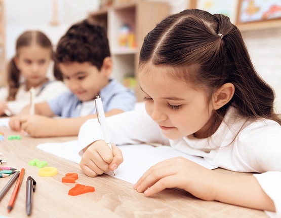 Children drawing and writing at classroom table