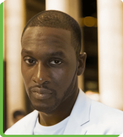 Portrait of a confident man in a white blazer with a blurred background.