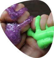 Hands squeezing green and purple glittery slime toys.