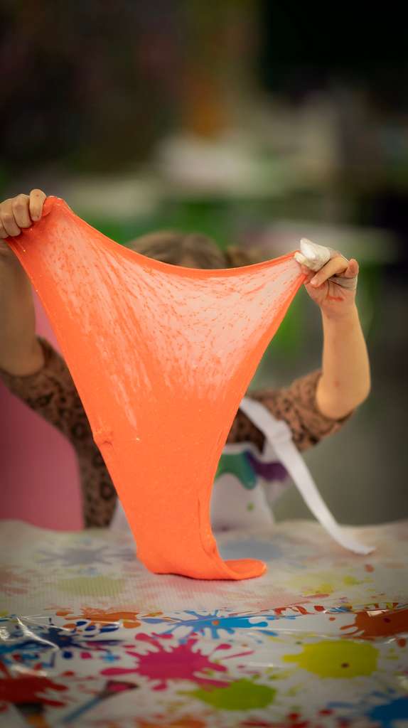 Hands stretching bright orange slime on table