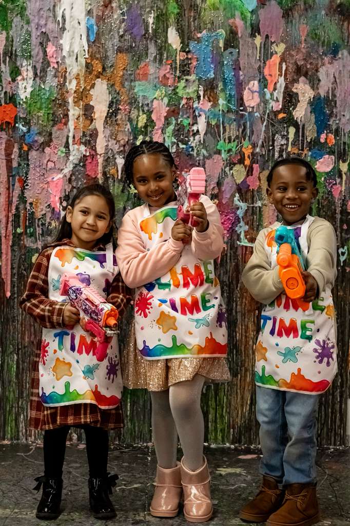 Three children with paint guns, colorful backdrop