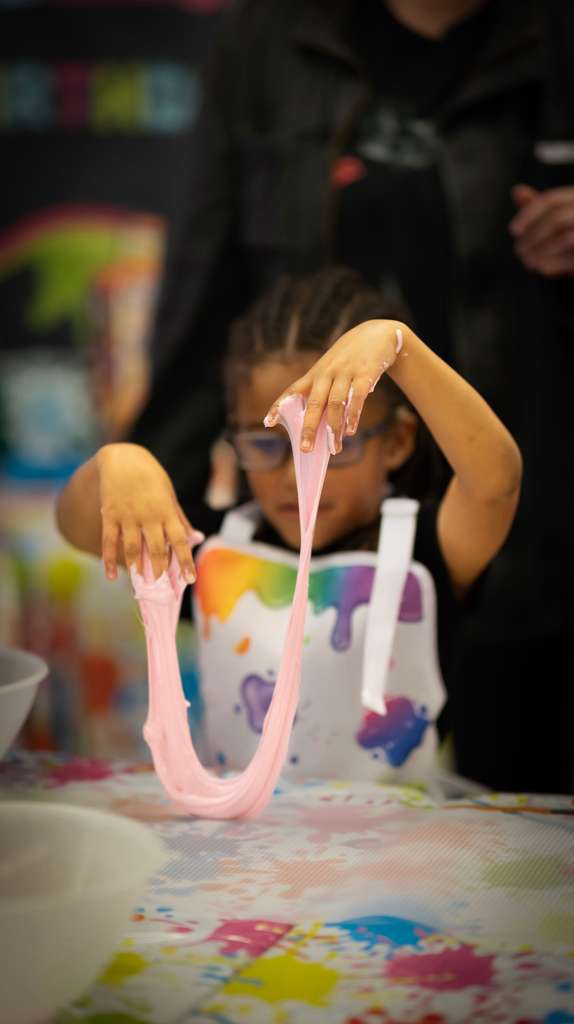 Child stretching pink slime at craft table